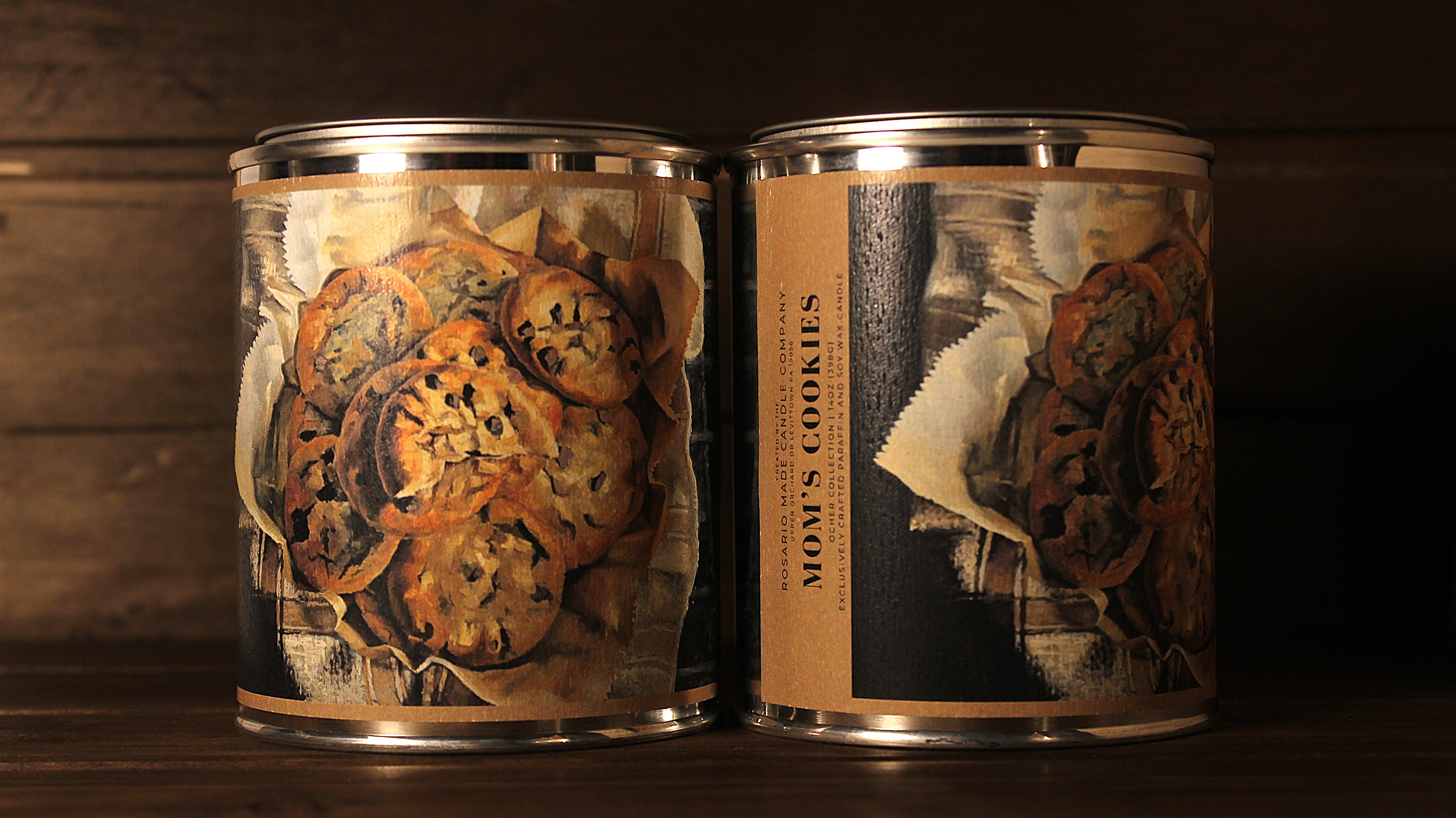 Two tin soy wax candles, a vanilla fragrance, with decorative labels of freshly baked cookies on a wooden surface.